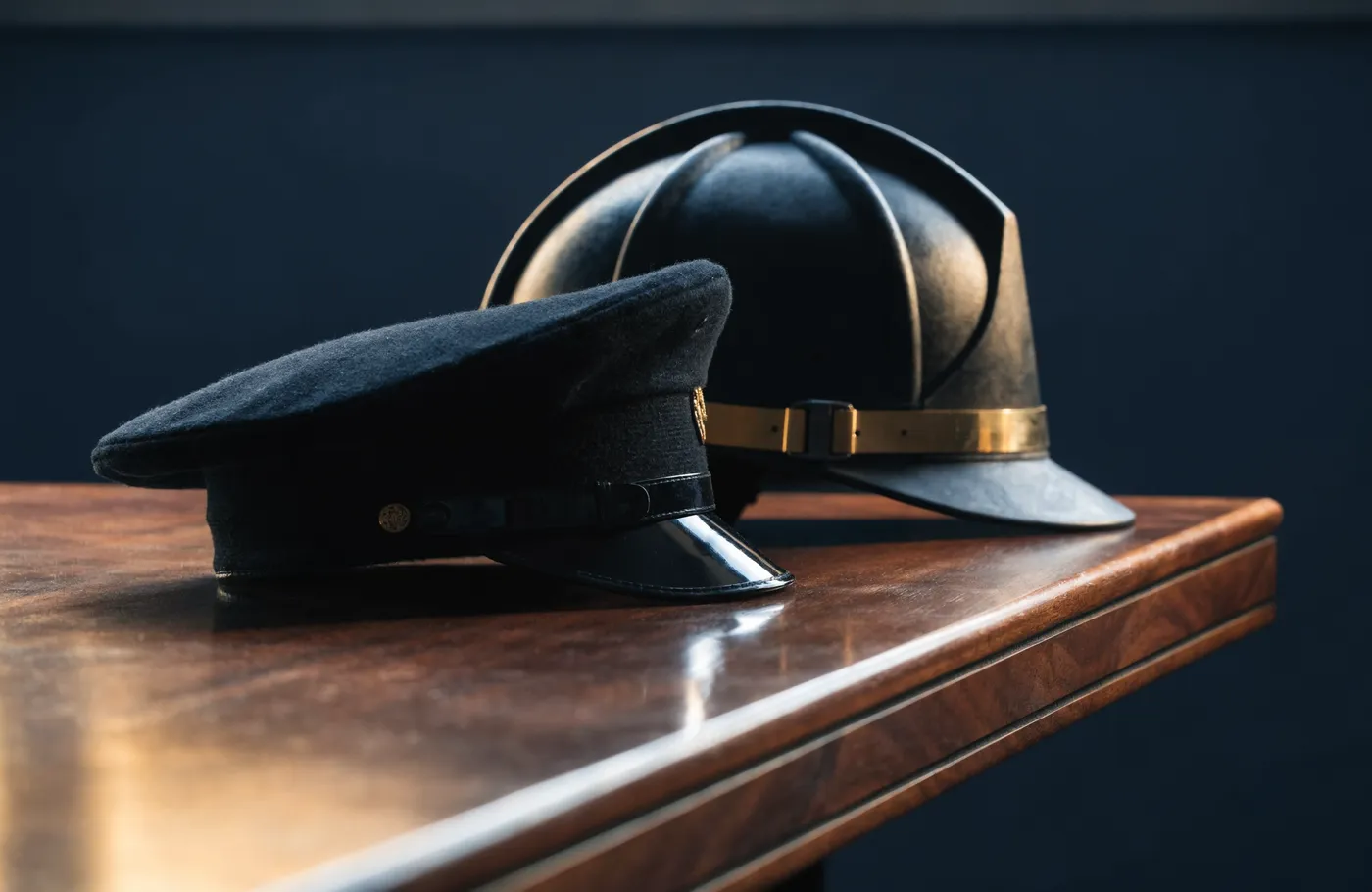 A firefighter's helmet and a police officer's cap resting together on a wooden table